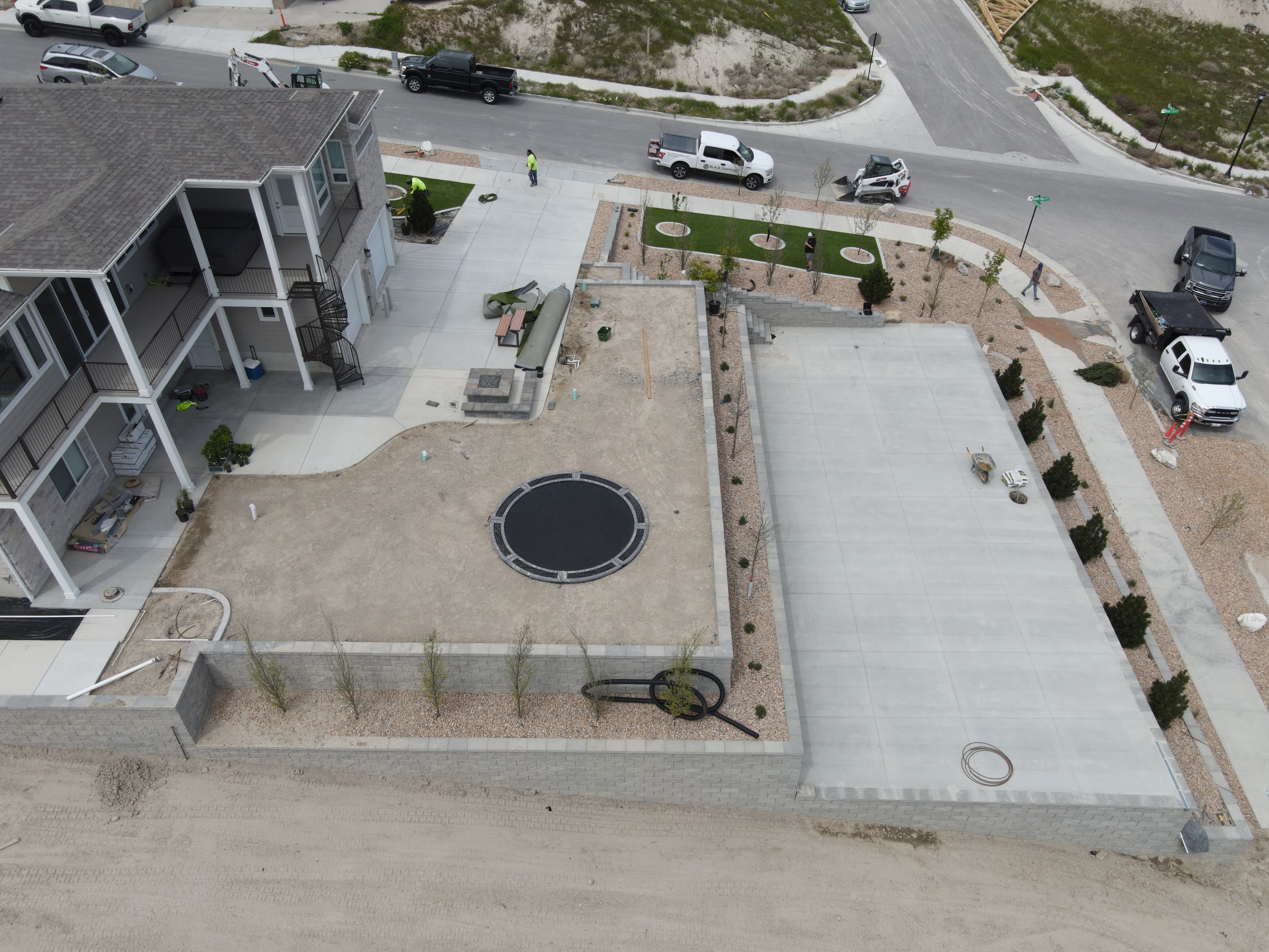 Aerial view of an active landscape construction site with concrete work, retaining walls, crews, and equipment — Salt Lake County, Utah