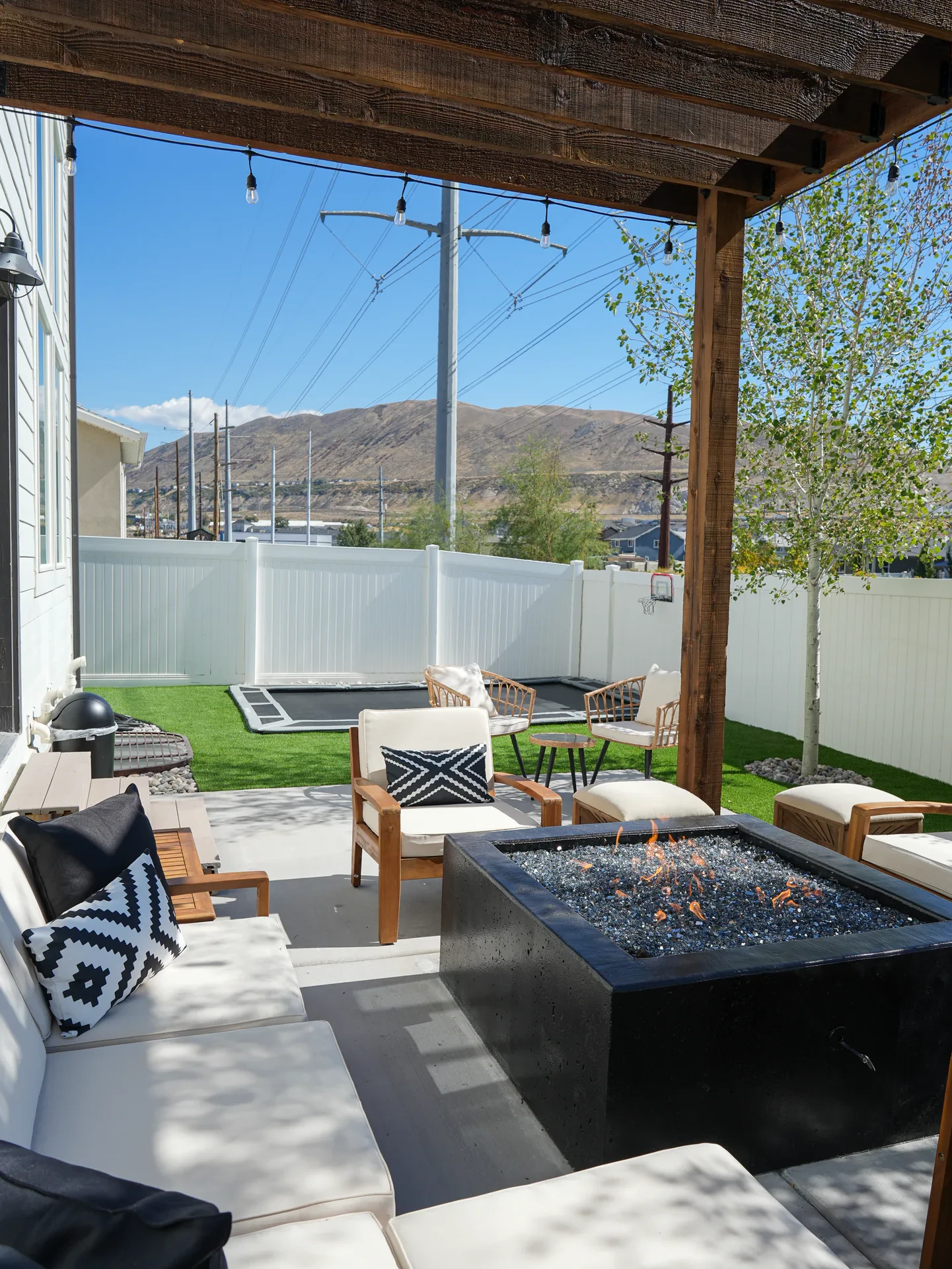 Custom square concrete fire feature beneath a wood pergola beside artificial turf in Bluffdale, Utah.
