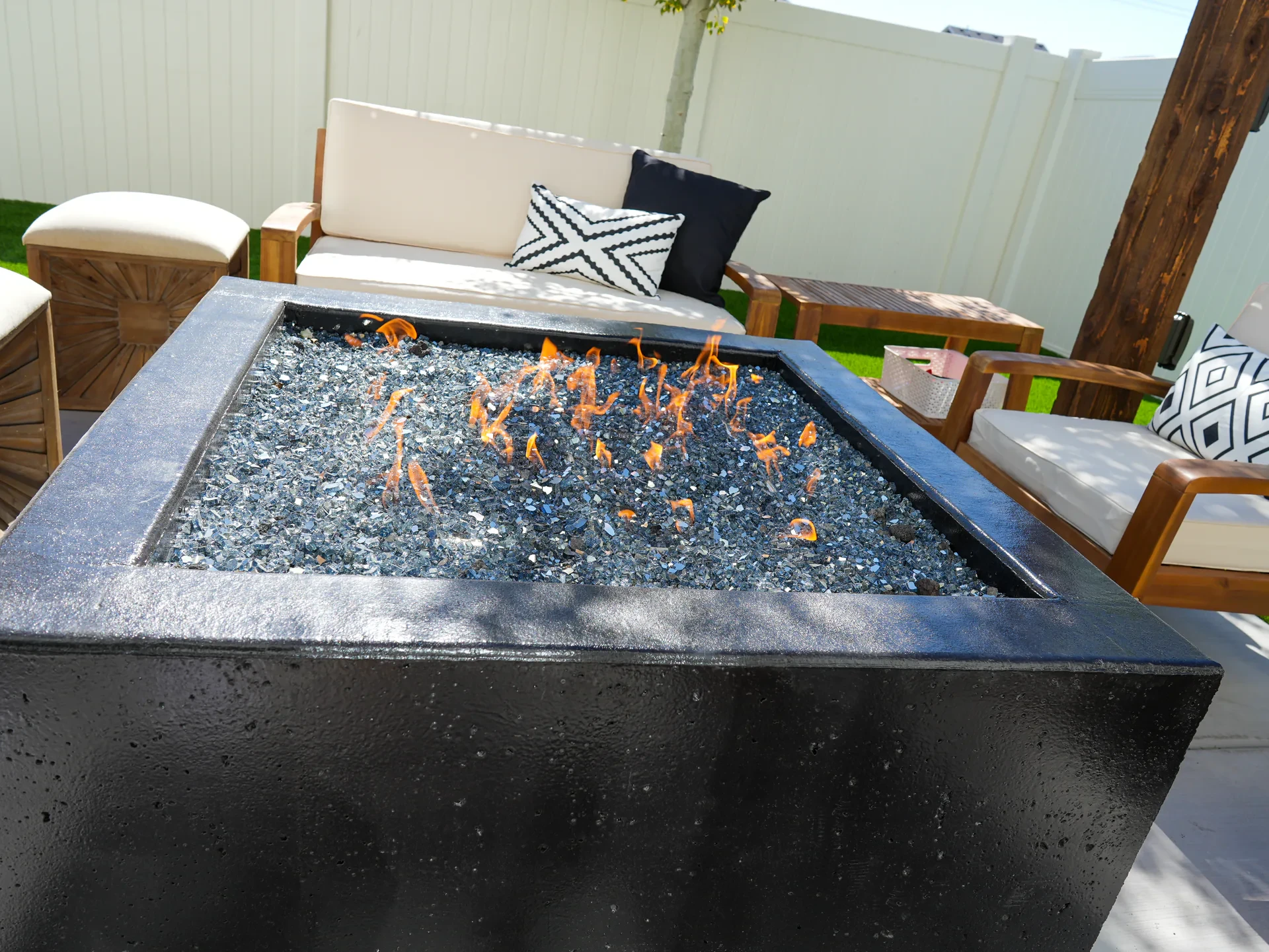 Square block fire feature with glass media on a concrete patio