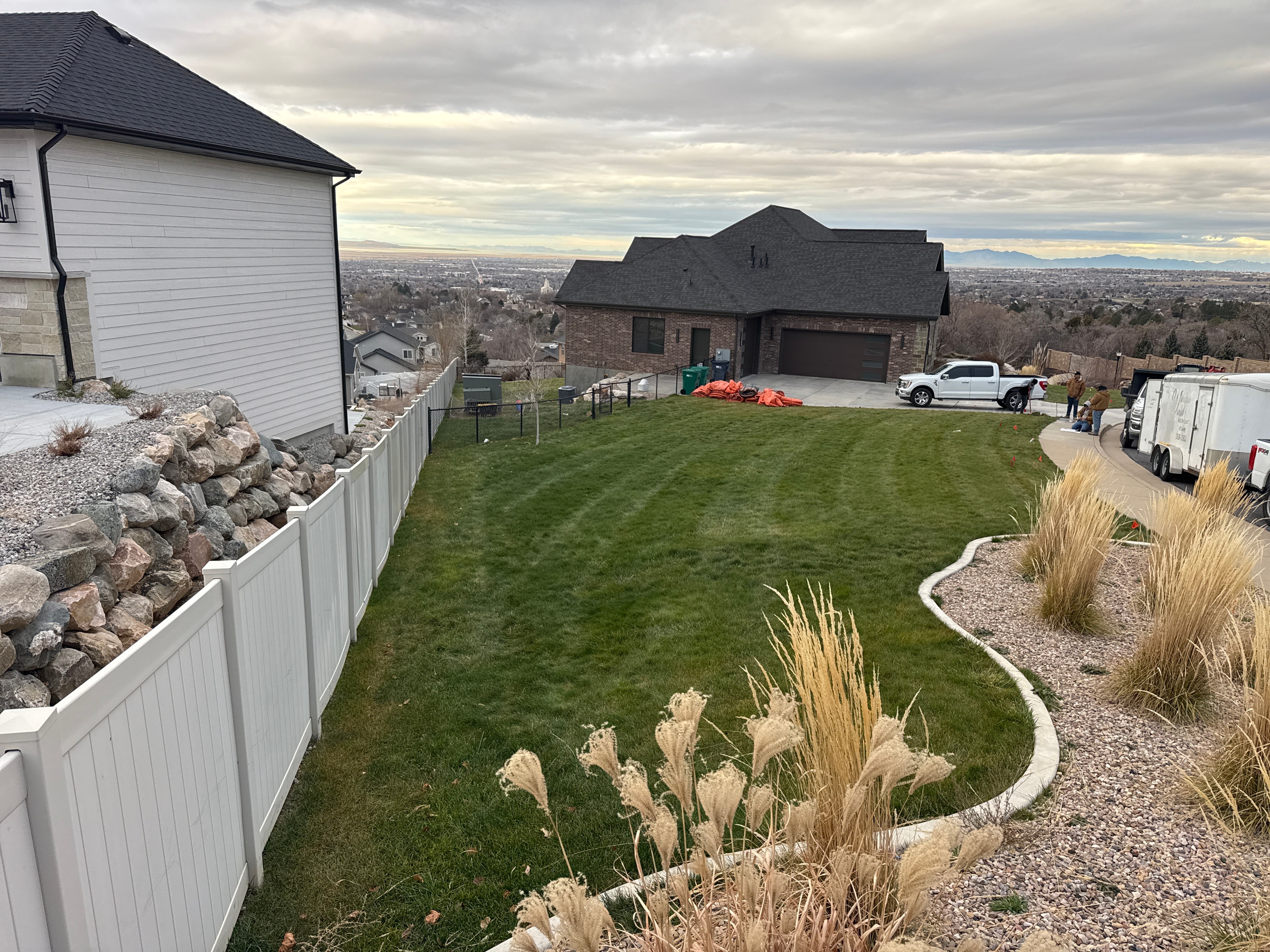 Sloped lawn and rock landscape beds before a complete outdoor living renovation in Layton, Utah