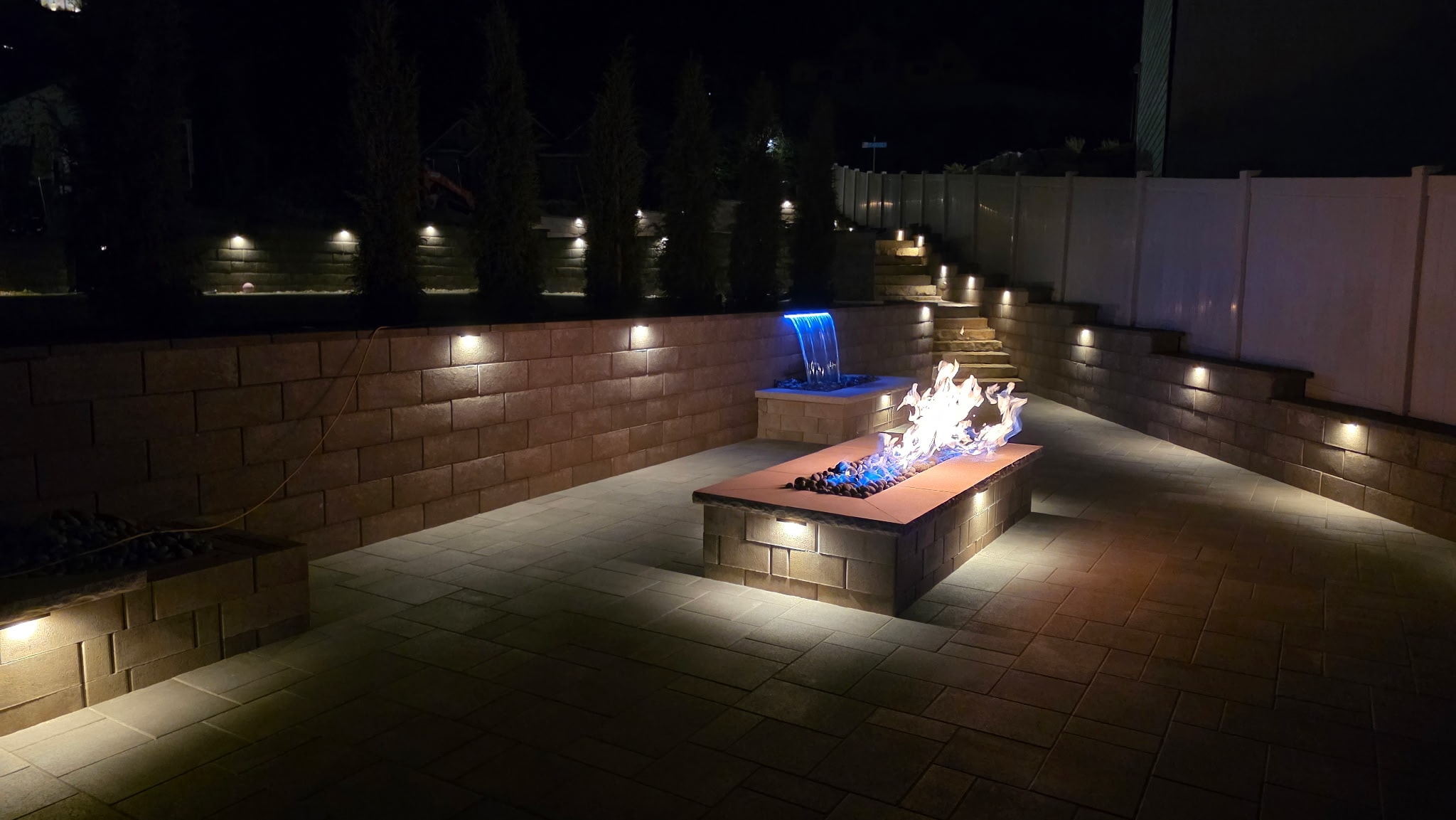 Custom linear fire feature and illuminated waterfall on a Belgard paver terrace in Layton, Utah