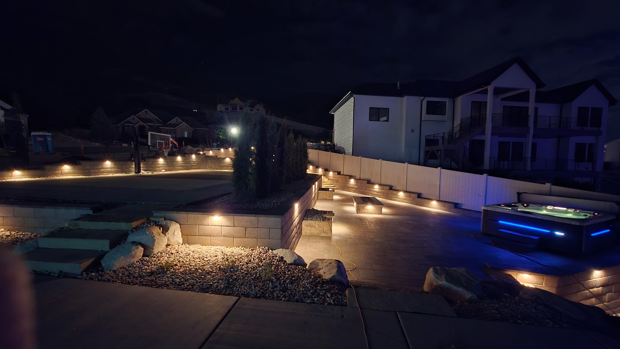 Illuminated Belgard paver patio, retaining walls and hot tub in a completed Layton outdoor living renovation at night