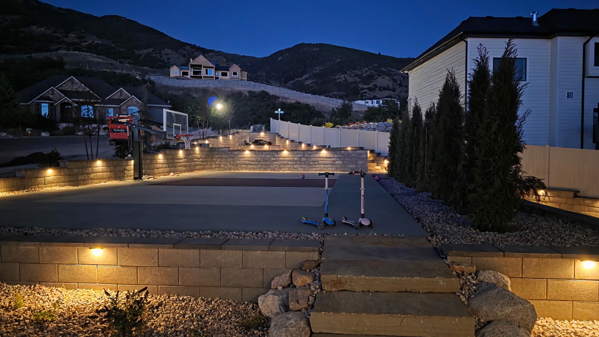Illuminated residential sport court, retaining walls and stone steps at night in Layton, Utah