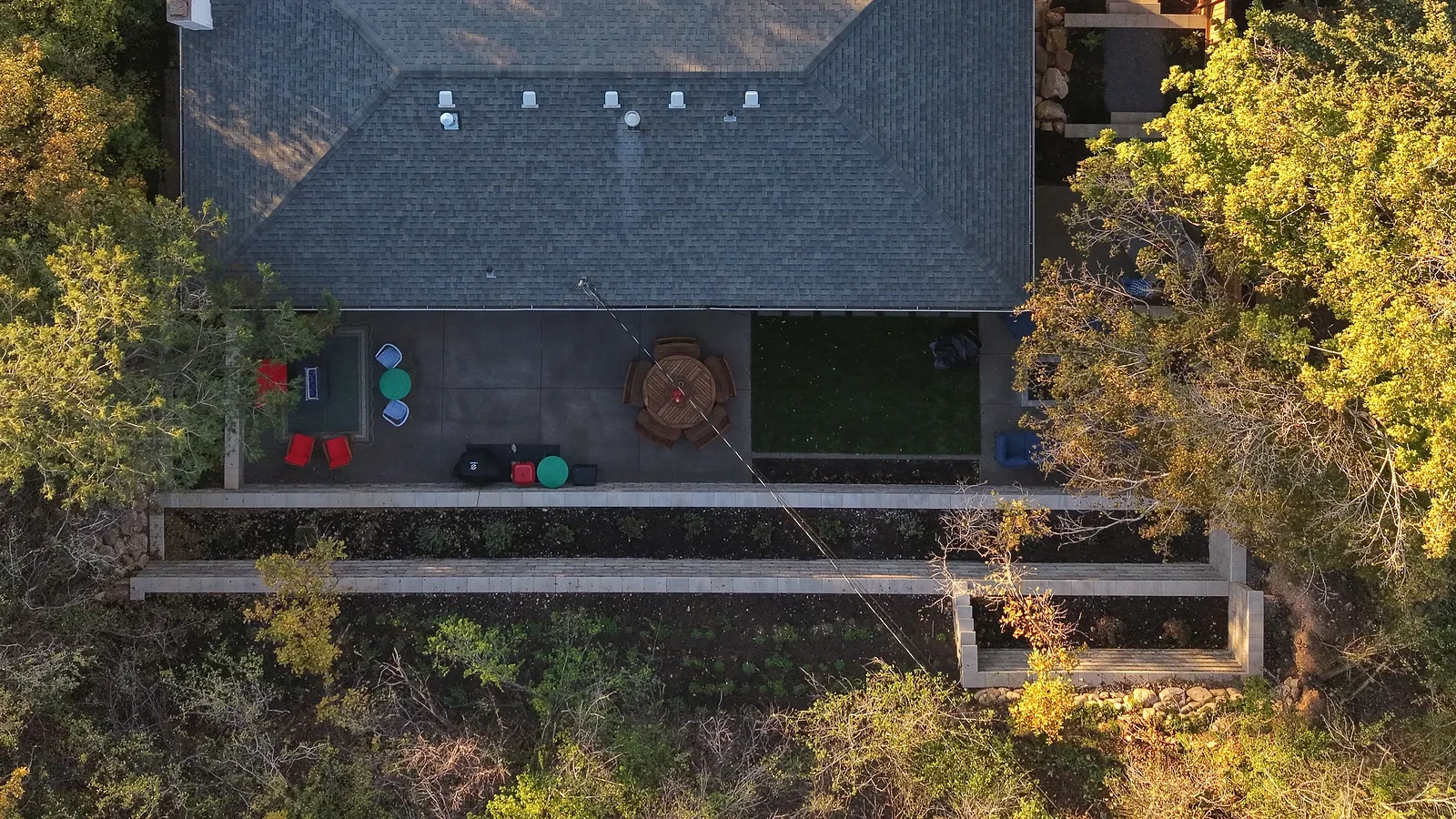 Overhead drone view of a rear patio, fire feature, turf and two terraced retaining walls behind an Olympus Cove home