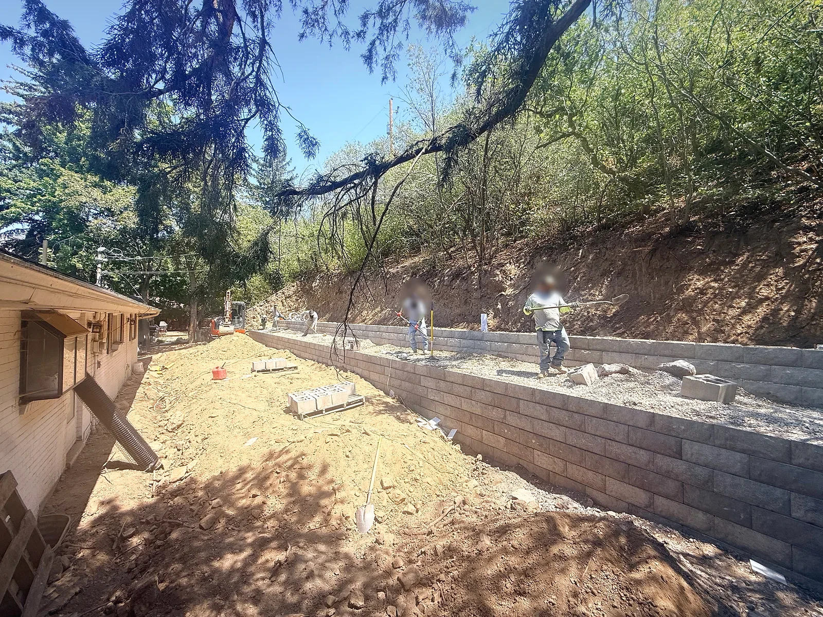 Crew building the upper terrace of a block retaining wall with gravel backfill