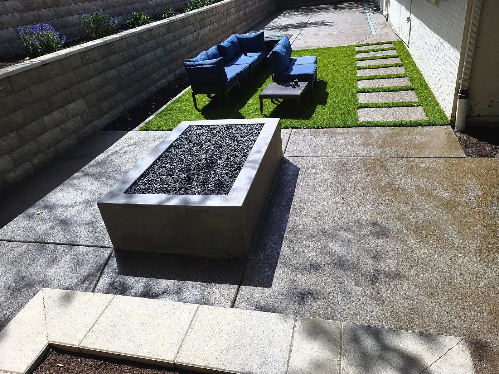 Rectangular polished concrete fire feature on a pewter exposed-aggregate patio next to turf and stepping pads