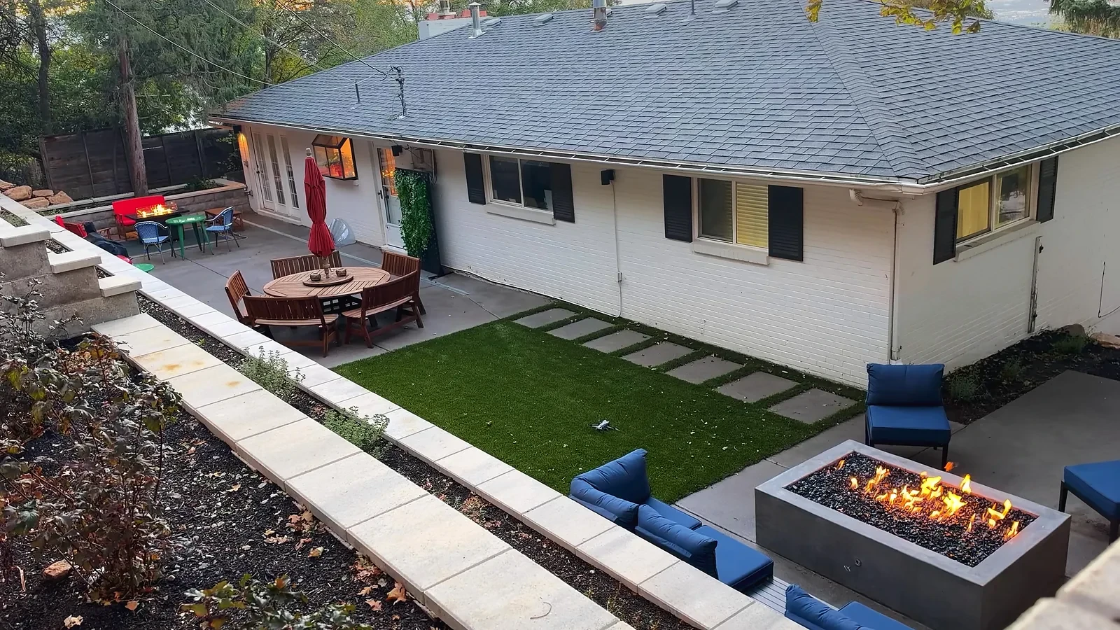 Polished concrete gas fire feature with flames and black fire glass beside turf and a dining patio