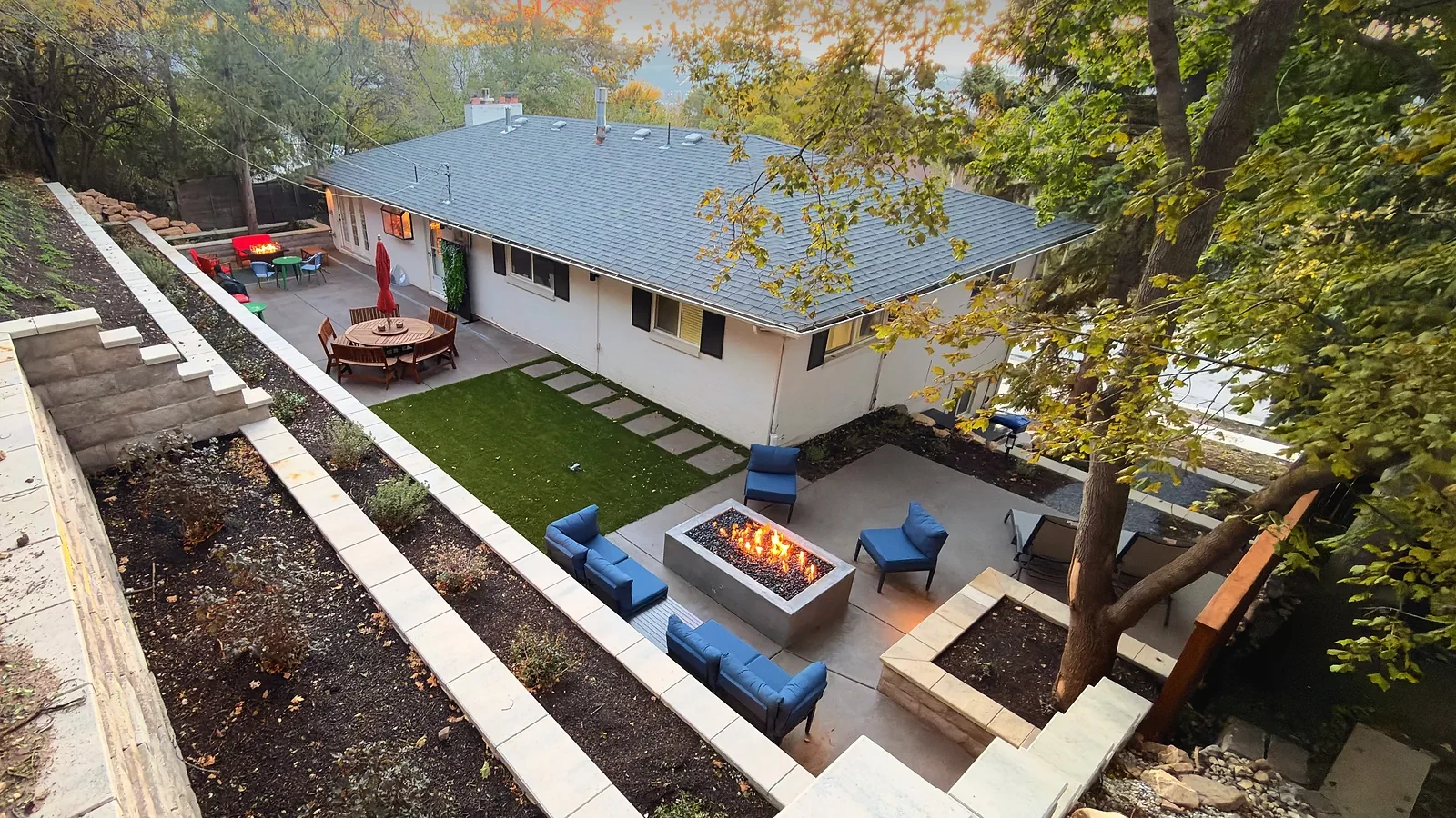 Elevated view of terraced block retaining walls, a concrete patio with a gas fire feature, and turf behind an Olympus Cove home