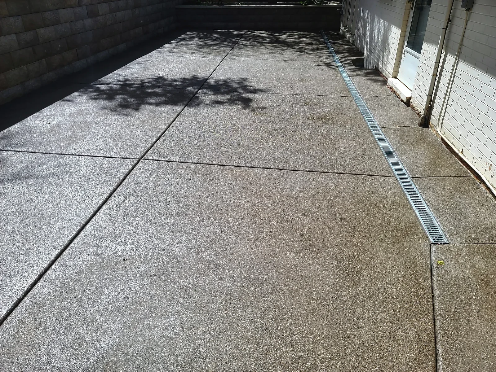 Pewter exposed-aggregate concrete patio with a trench drain running along the house