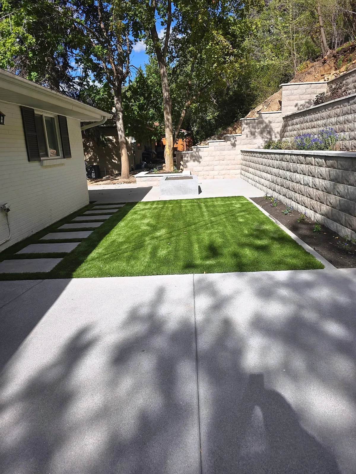 Side yard with MSI Verdura Gold turf, concrete stepping pads and terraced block walls along an Olympus Cove home