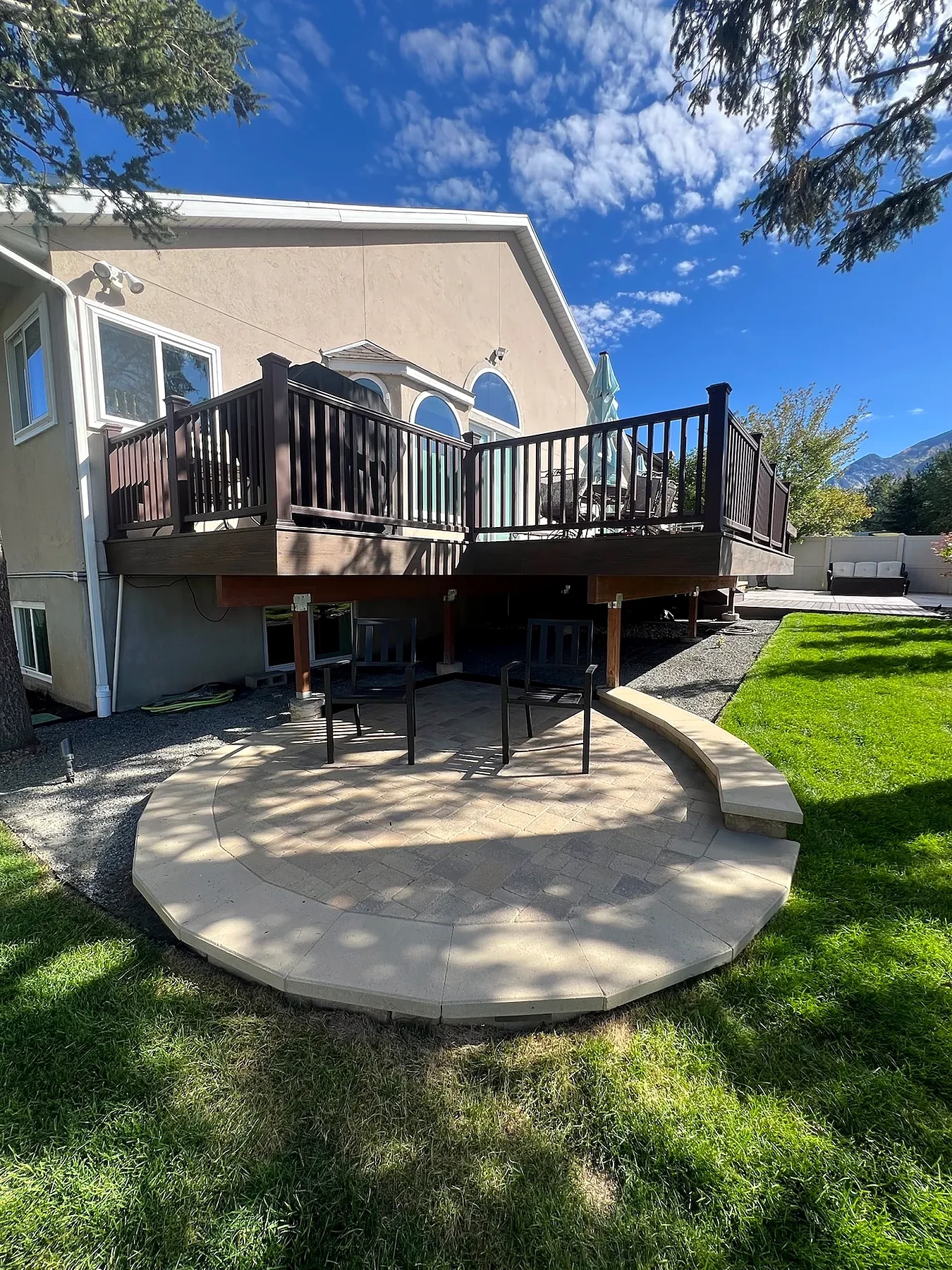 Circular Belgard paver patio with seat wall under a raised deck in a Sandy backyard