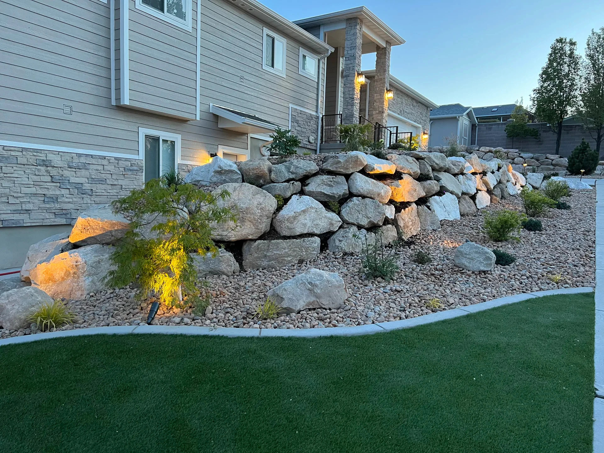 Natural boulder wall with custom concrete curbing and lawn edge in South Jordan, Utah.