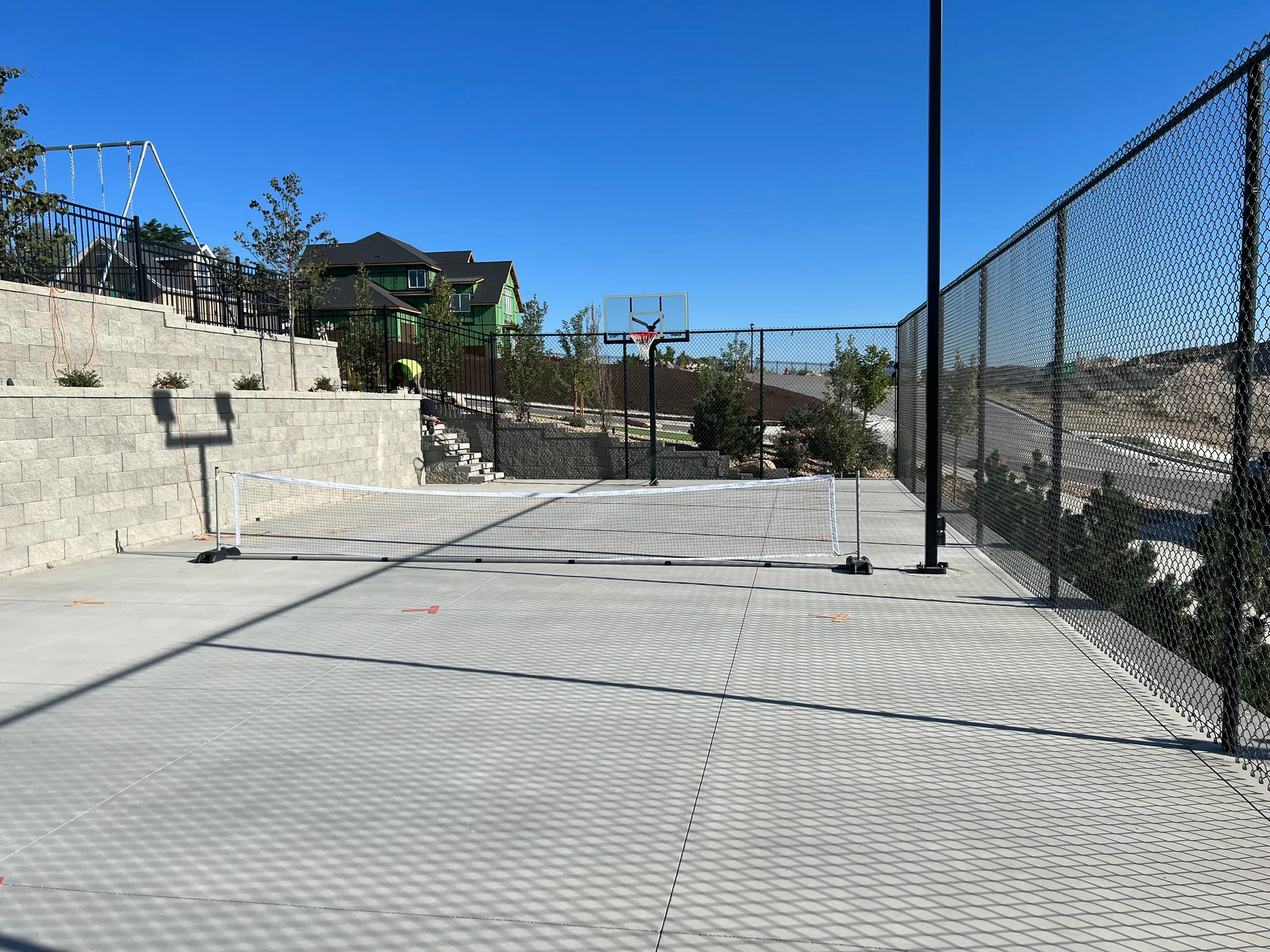 Custom concrete sport court with basketball hoops, perimeter fence and retaining walls in South Jordan, Utah.