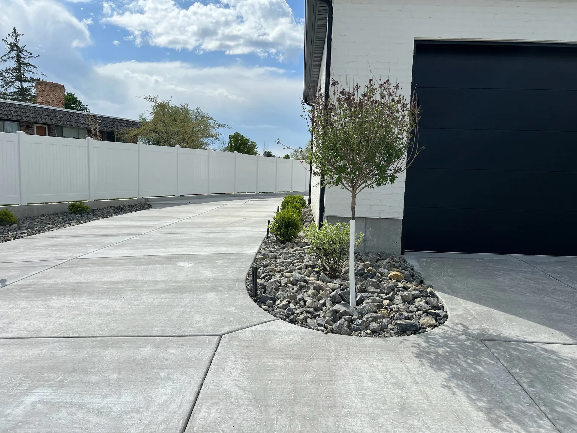 Curved concrete driveway edge with decorative-rock planting island and early tree planting in West Valley City