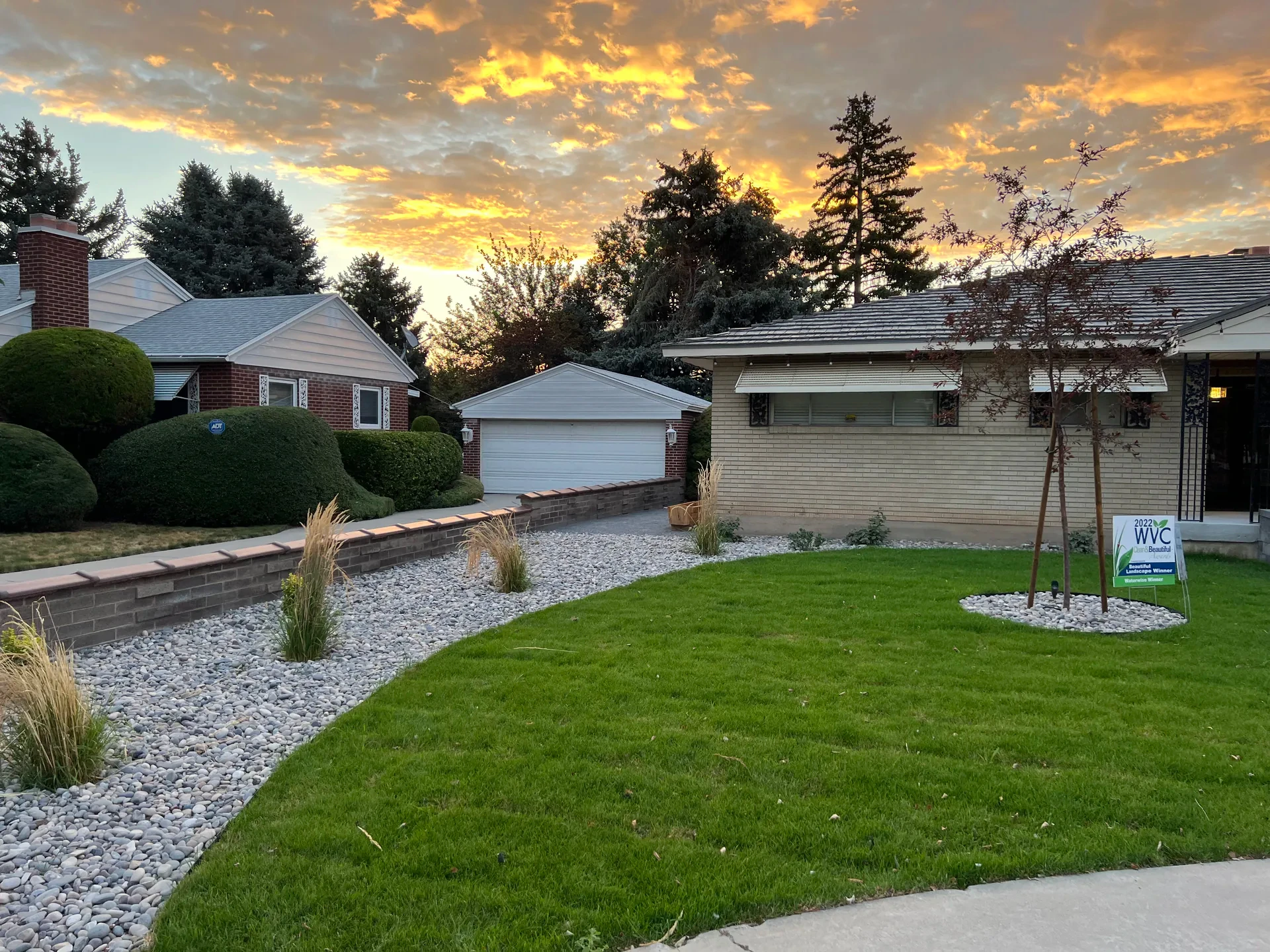 Completed West Valley City front landscape with lawn, decorative stone, planted beds and a renovated entry at sunset