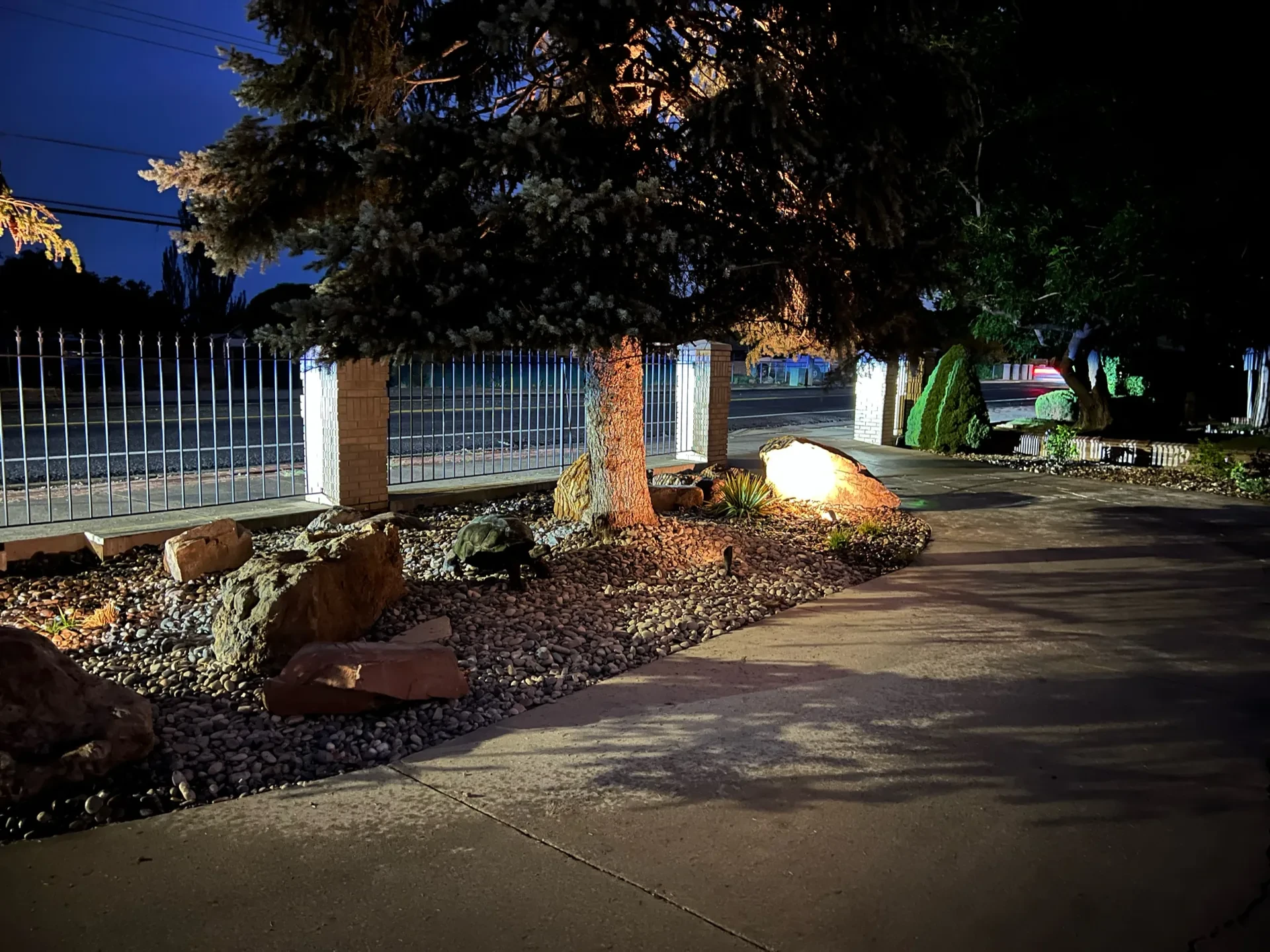 Warm low-voltage uplighting on mature trees beside decorative stone and water-wise planting in West Valley City
