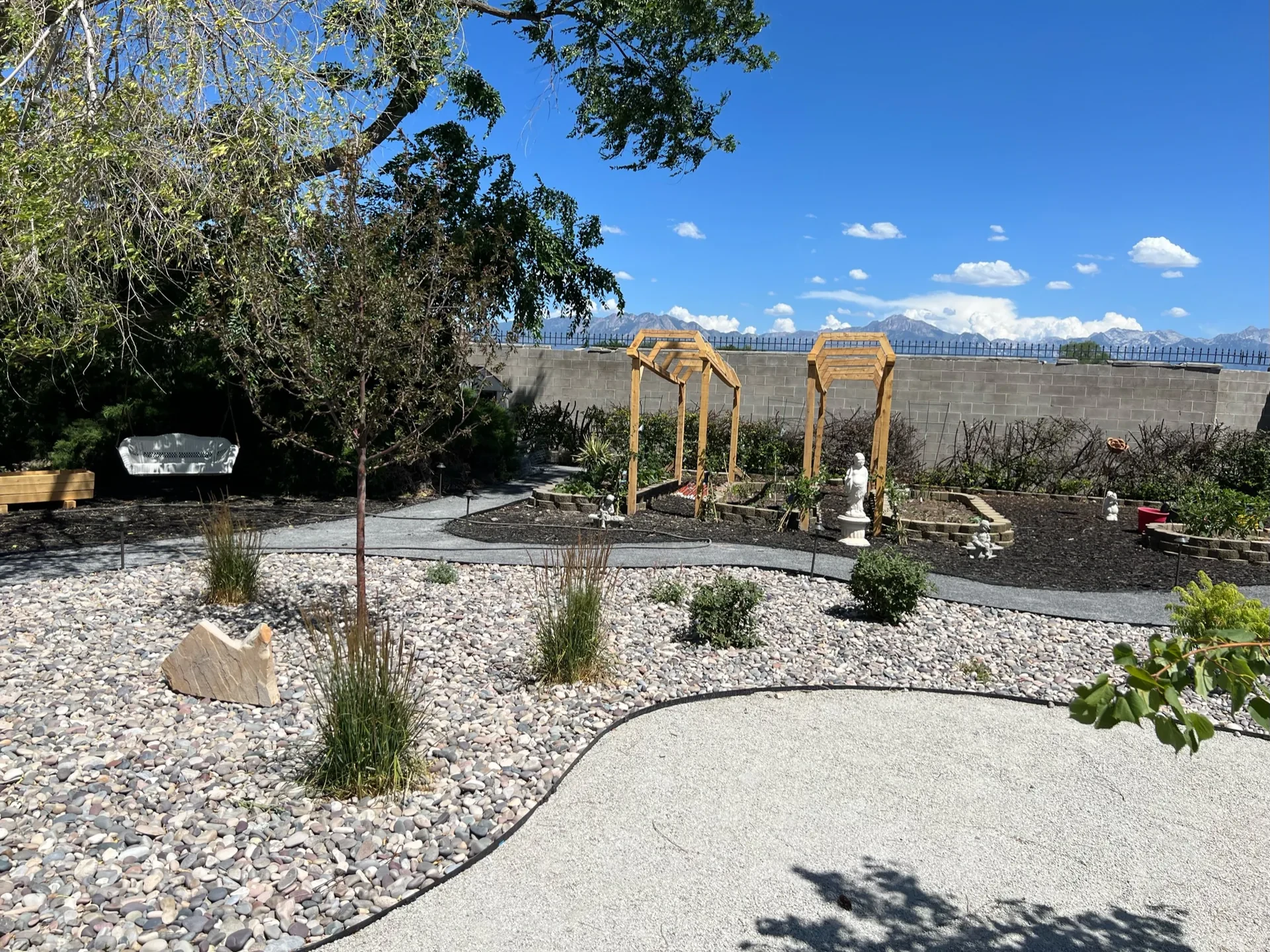 Pergola and outdoor gathering area surrounded by decorative stone and layered planting in West Valley City