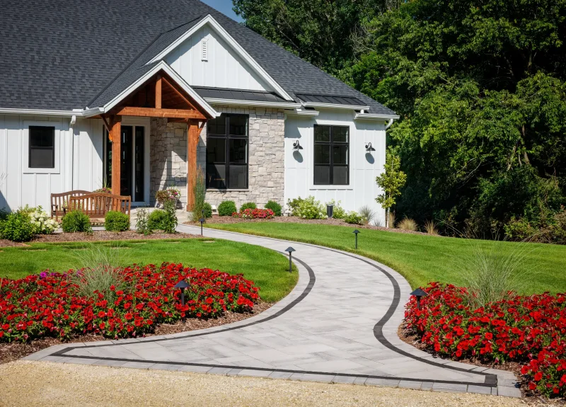 Belgard Dimensions 12 curved walkway with Brooklyn Paver dark border, red flower beds, and path lighting at modern farmhouse entry — manufacturer inspiration.