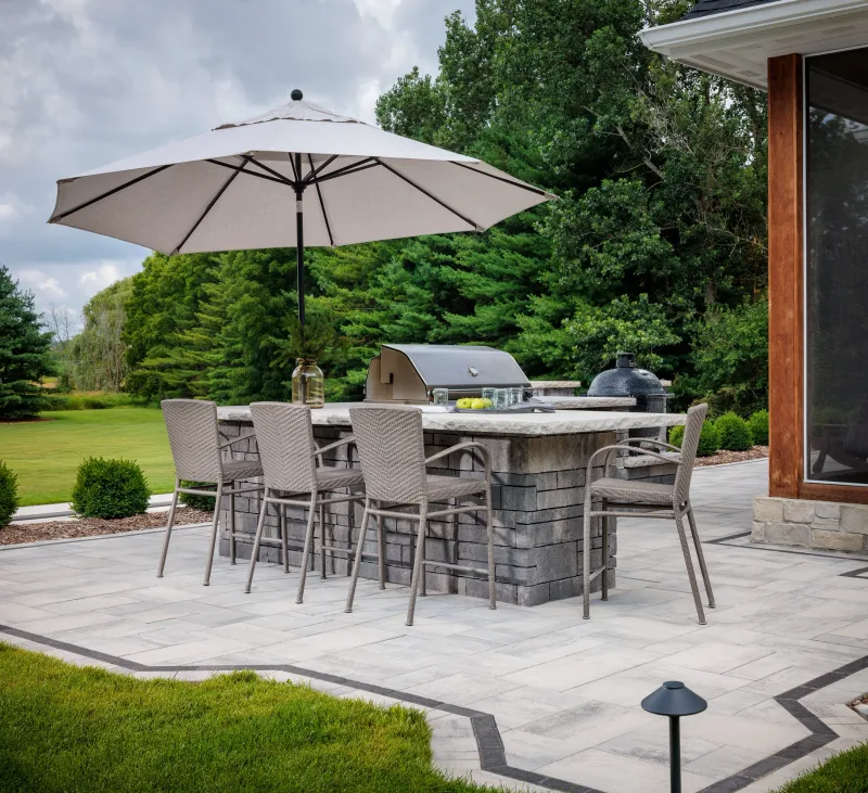 Belgard outdoor kitchen bar with Artforms counter, Ashlar Tandem Wall surround, Dimensions 12 paver field with Brooklyn Paver border, and Kamado grill — manufacturer inspiration.