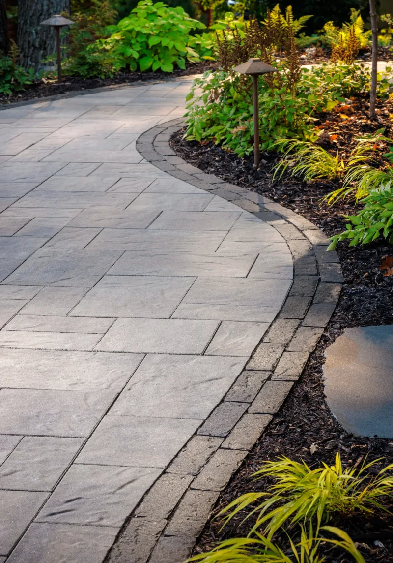 Belgard Origins 12 curved pathway with Brooklyn Paver border and low-voltage path lighting — manufacturer inspiration.
