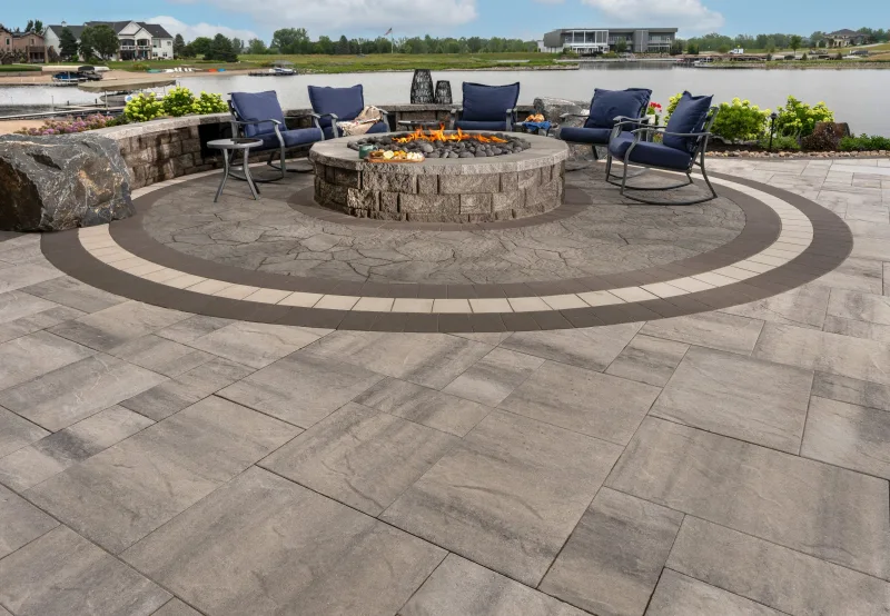 Belgard Origins 12 waterfront patio with Dimensions 6x9 accent banding and Highland Stone circular fire pit surround — manufacturer inspiration.