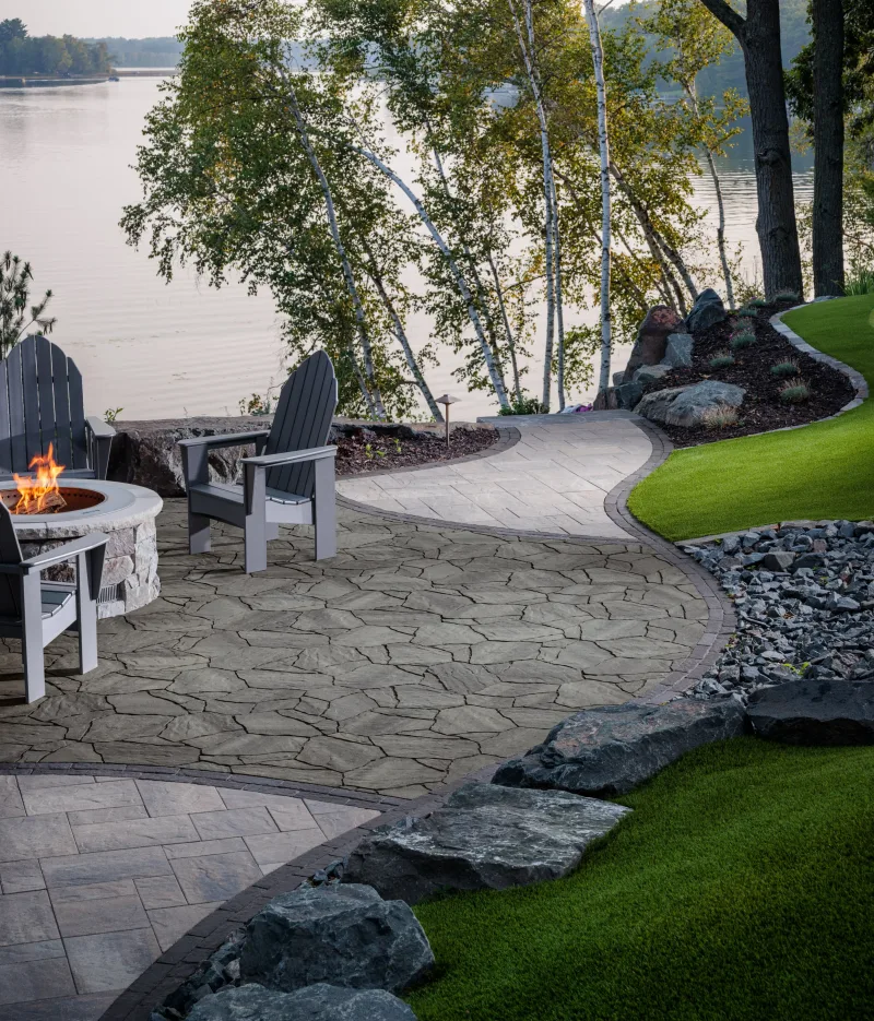 Belgard MegaArbel Newport Gray lakefront patio with Origins 12 lower terrace, Brooklyn Paver border, and fire pit — manufacturer inspiration.