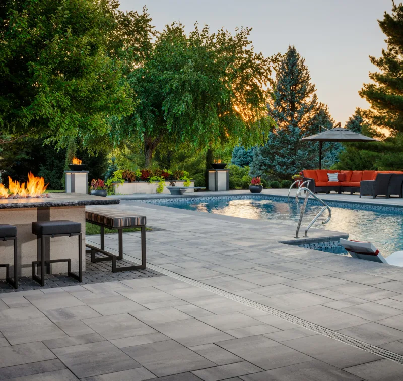 Belgard Dimensions 18 Old York poolside patio with Artforms fire bar and pedestal fire bowls at golden hour — manufacturer inspiration.