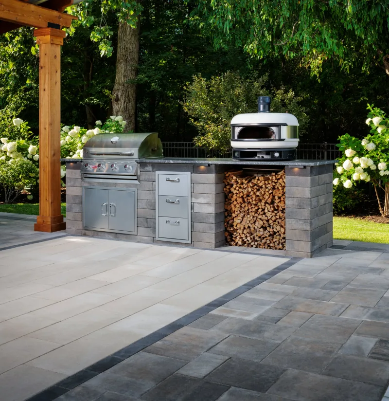 Belgard outdoor kitchen under cedar pergola with DimensionsSlab 12x24 floor, Dimensions Accent 6x9 border, and Melville Wall surround — manufacturer inspiration.